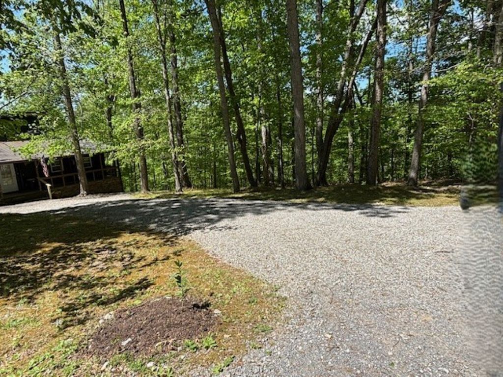 Sorapäällysteinen pysäköintialue, jonka vasemmalla puolella on rakennus ja taustalla metsäinen alue.