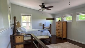 Une chambre à coucher avec un lit, une commode en bois, un ventilateur de plafond et une fenêtre.