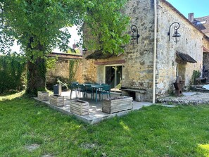 Un bâtiment en pierre doté d’une terrasse, de sièges extérieurs et d’un arbre.