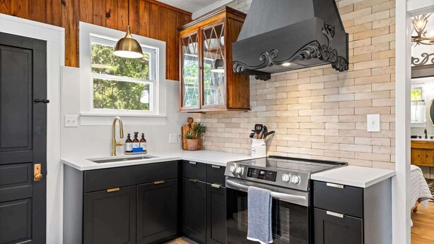 Une cuisine avec des meubles de couleur sombre, une cuisinière en acier inoxydable et une fenêtre donnant sur un paysage verdoyant.