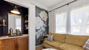 Un salon comprenant un canapé, une table basse, un meuble avec un miroir et une grande fresque murale représentant des motifs floraux.