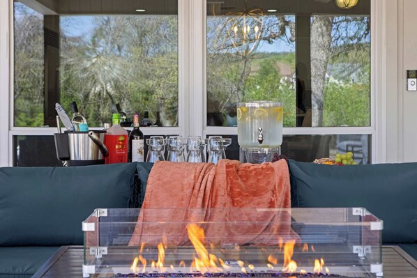 Habitación con sofá, una mesa de vidrio con chimenea y ventana con vista a árboles y un edificio.