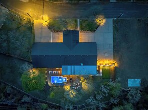 An aerial view of a house with a swimming pool, a garage, and a well-lit driveway. - Enchanted Vine - Pool, Spa, Sauna & Speakeasy (Fredericksburg)