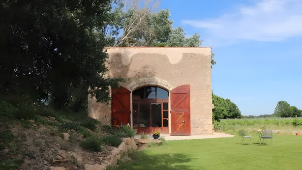 Un bâtiment rustique avec une façade en pierre, une grande entrée en arc de cercle et une pelouse verdoyante.