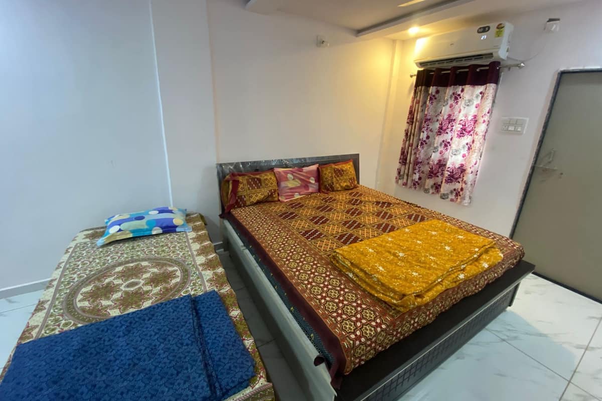 A bedroom with a bed, a bedside table, a wall-mounted air conditioner, and a curtain.
