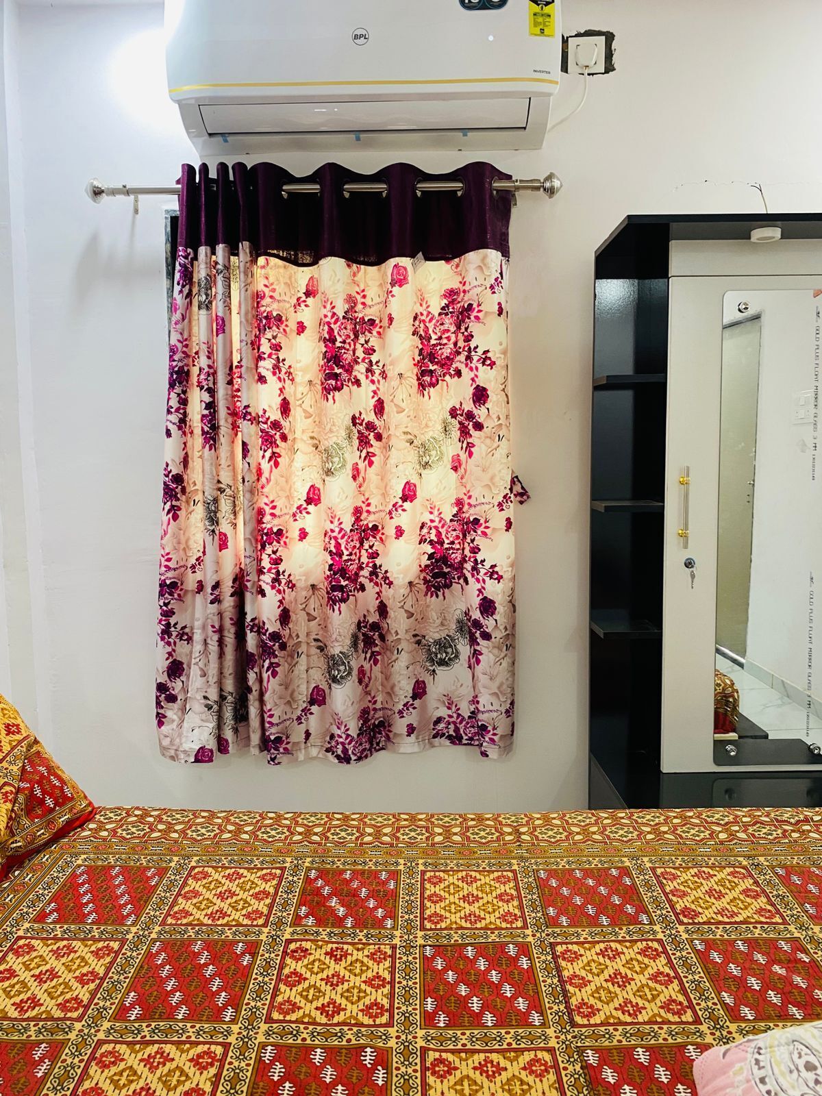 Una habitación con cama, aire acondicionado de pared, espejo y colcha estampada.
