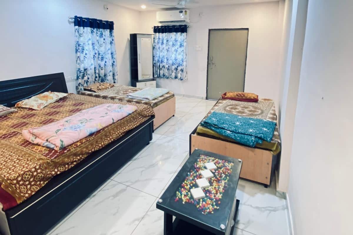 A bedroom with two beds, a ceiling fan, an air conditioning unit, and a small table with colorful objects.