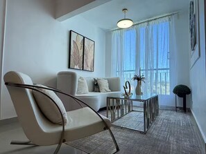 A modern living room with a sofa, a chair, a coffee table, and a large window with curtains. - Modern penthouse with Jacuzzi near the airport (Santiago de los Caballeros)