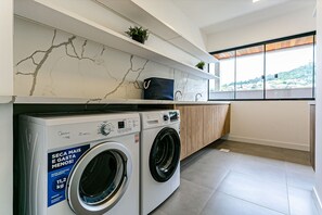 Ein moderner Waschraum mit Waschmaschine, einer Arbeitsplatte mit Pflanze und Blick durch ein großes Fenster.