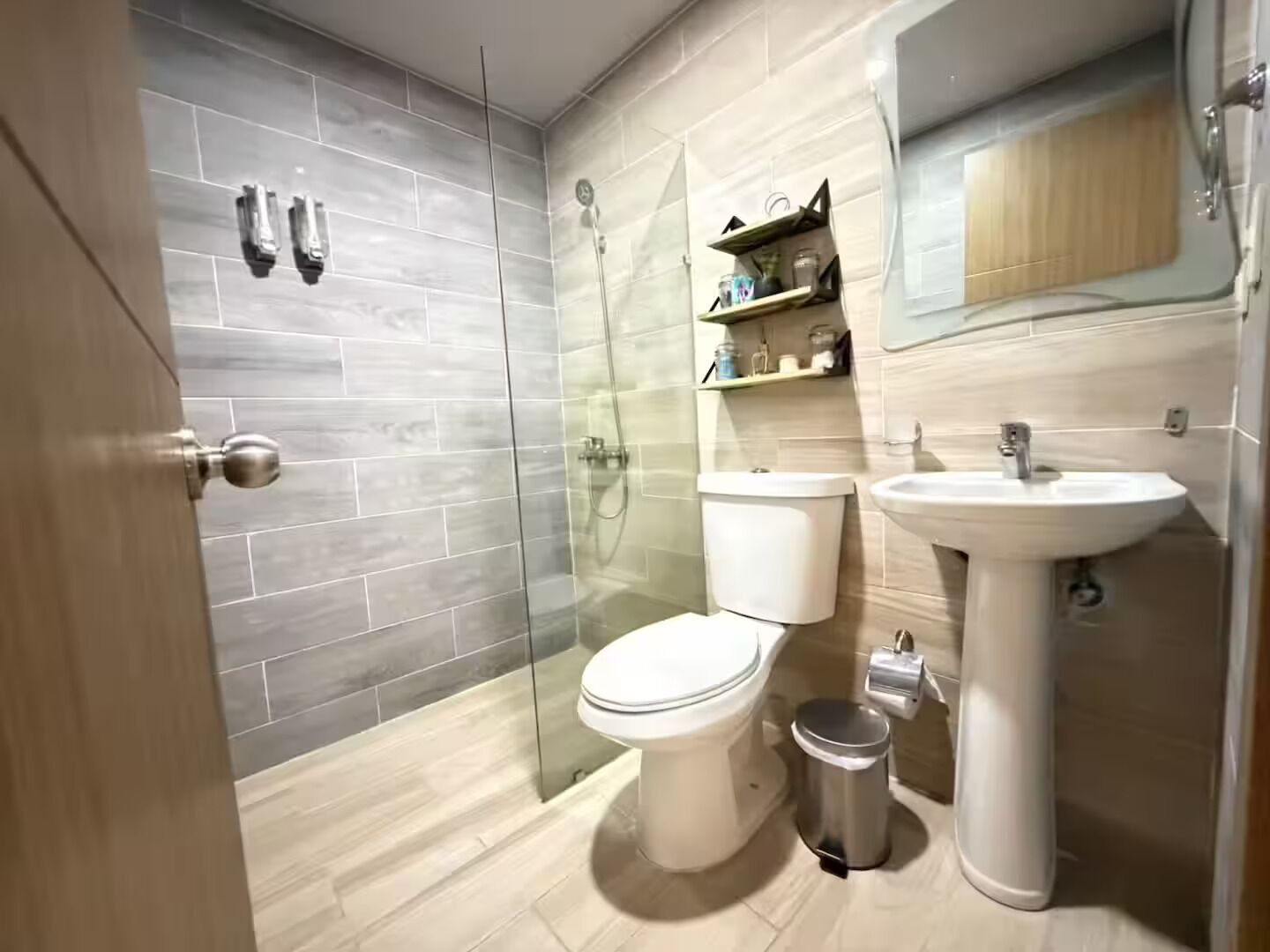 Un baño moderno con ducha envuelta en vidrio, inodoro, lavabo y un pequeño cubo de basura.