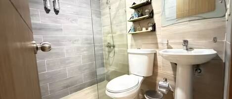 Un baño moderno con ducha envuelta en vidrio, inodoro, lavabo y un pequeño cubo de basura.