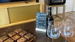 Un coin bar avec un téléviseur, une bouteille de vin, deux verres et un tableau affichant le menu.