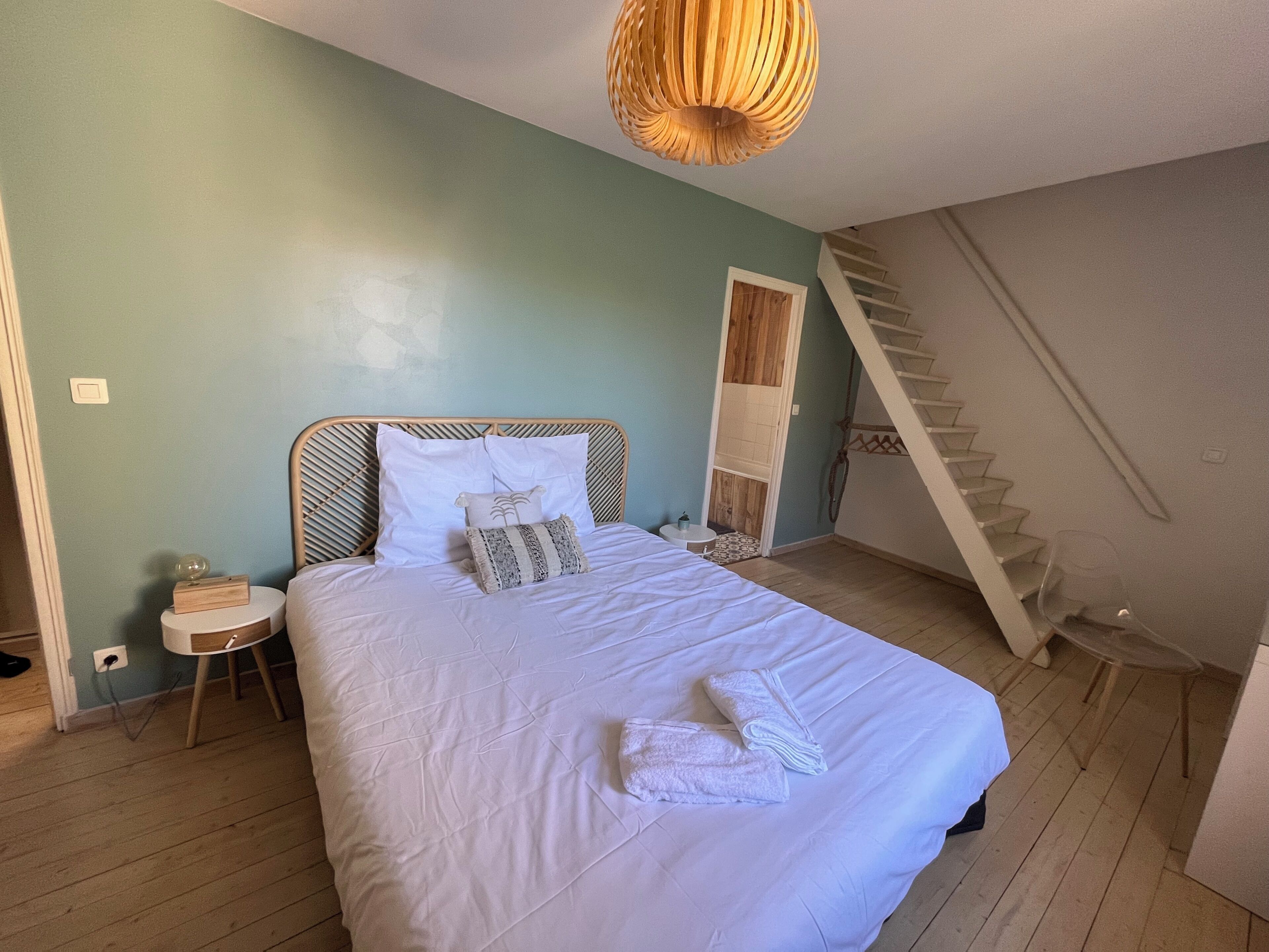 Une chambre à coucher comprenant un lit, une table de chevet, une tête de lit en bois, un escalier et un luminaire suspendu.