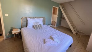 Une chambre à coucher comprenant un lit, une table de chevet, une tête de lit en bois, un escalier et un luminaire suspendu.