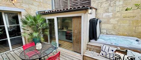 A patio with a table and chairs, a hot tub, and a wooden deck.