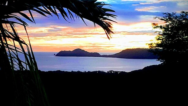 A coastal landscape with a sunset, palm trees, and distant islands.