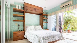 A bedroom with a bed, wooden shelving, a nightstand, and a window with a view of greenery. - Room-tranquil Poolside Retreat in Playa (Sardinal)
