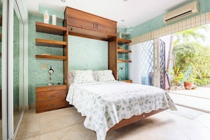 A bedroom with a bed, wooden shelving, a nightstand, and a window with a view of greenery. - Room-tranquil Poolside Retreat in Playa (Sardinal)