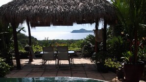 A clear pool with a thatched roof structure, lounge chairs, and potted plants. - Room-tranquil Poolside Retreat in Playa (Sardinal)