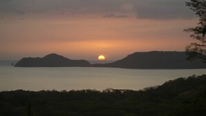 A sunset over water with landforms in the distance. - Room-tranquil Poolside Retreat in Playa (Sardinal)