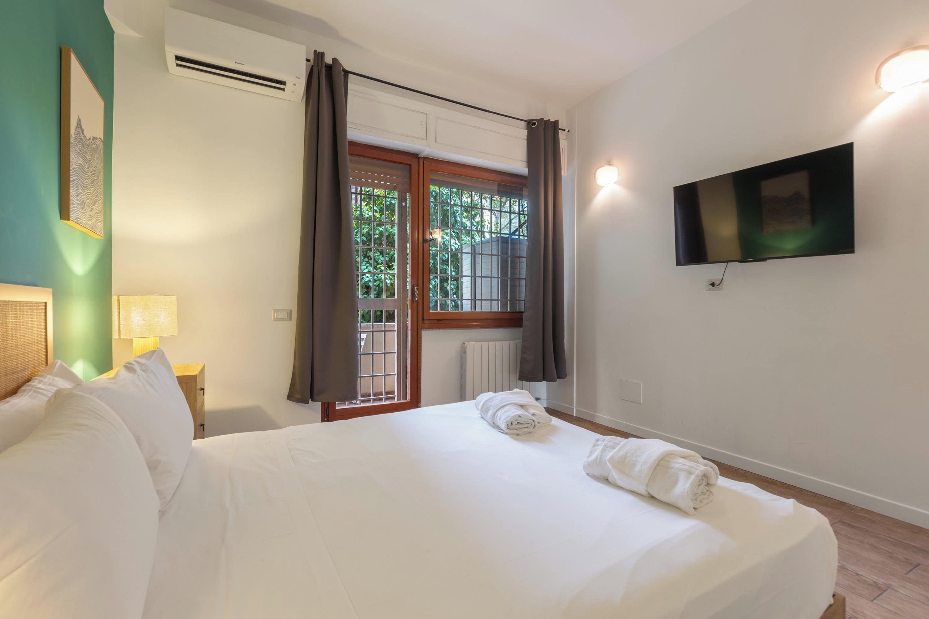 A hotel room with a bed, a television mounted on the wall, and a window with curtains.