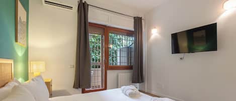 A hotel room with a bed, a television mounted on the wall, and a window with curtains.