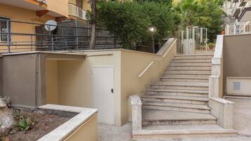 Unos escalones de piedra conducen a la entrada de un edificio, con una puerta y una pequeña zona ajardinada a la izquierda.