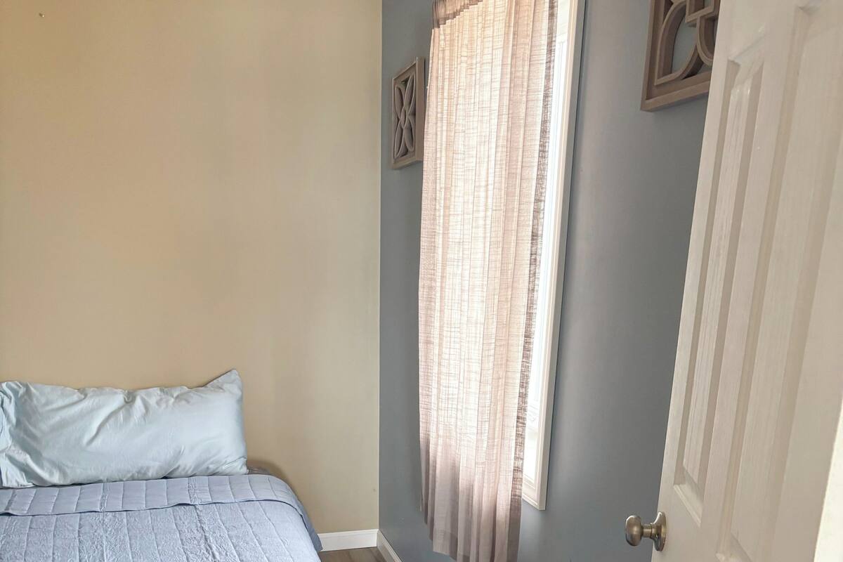 A bedroom with a bed, a door, and a window with curtains.