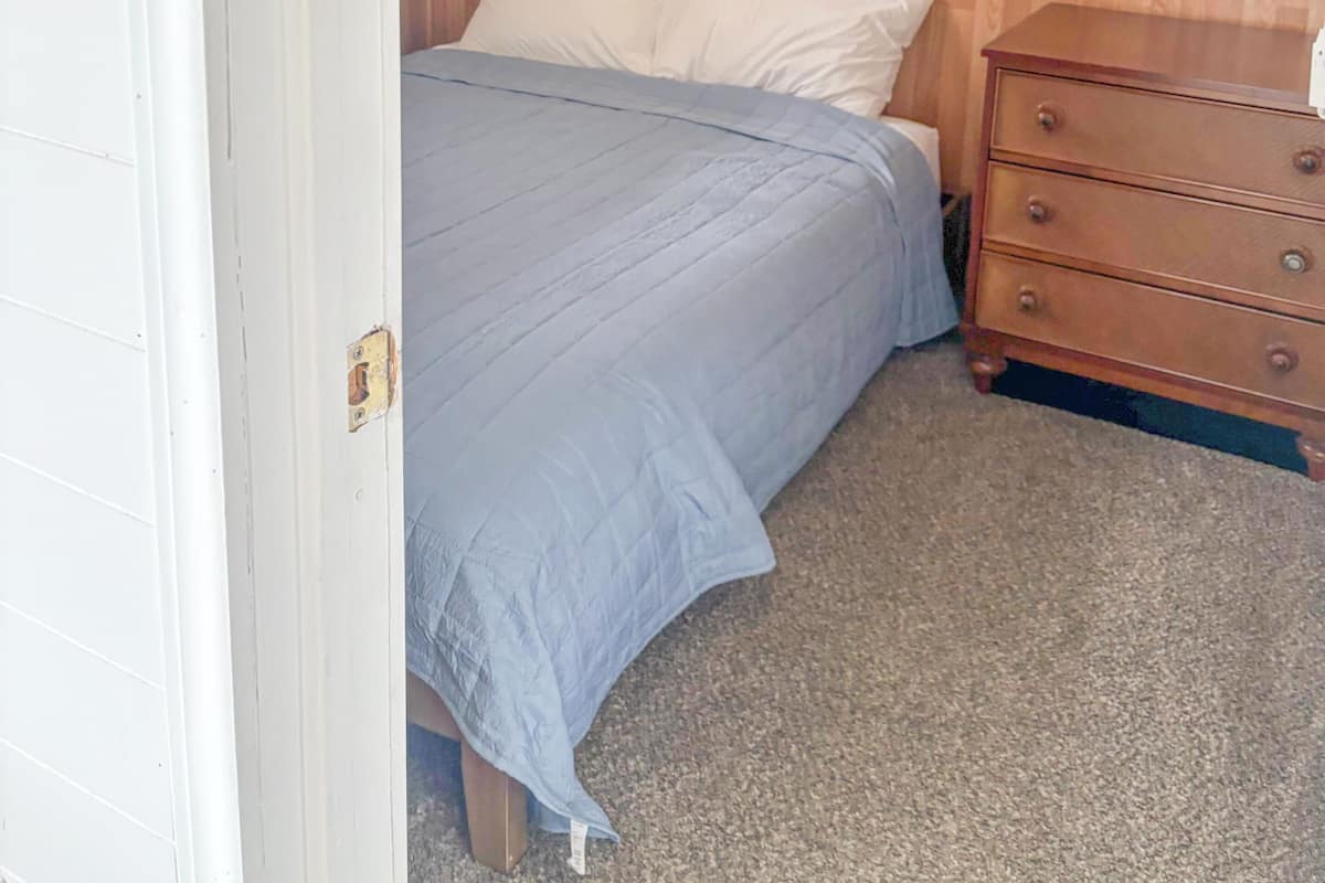 A bedroom with a wooden headboard, a bed with a blue bedspread, a wooden dresser, and three framed pictures on the wall.