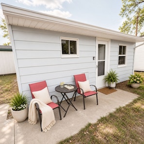 A single-story house with a front porch, two chairs, a small table, and potted plants. - Sunkissed Resort (Oscoda)