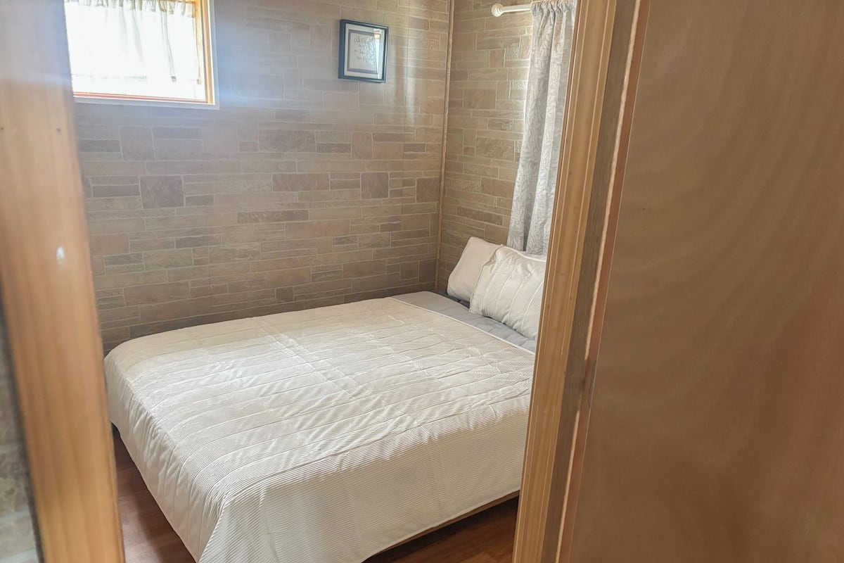 A bedroom with a brick wall, a bed with a white bedspread, a window with curtains, and a framed picture on the wall.