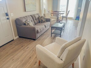 A living room with a sofa, armchair, coffee table, and a dining area with chairs and a table. - Sunkissed Resort (Oscoda)