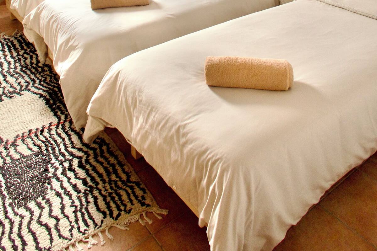 Ein Hotelzimmer mit drei Betten, einem gemusterten Teppich und einem Fenster mit Vorhängen.