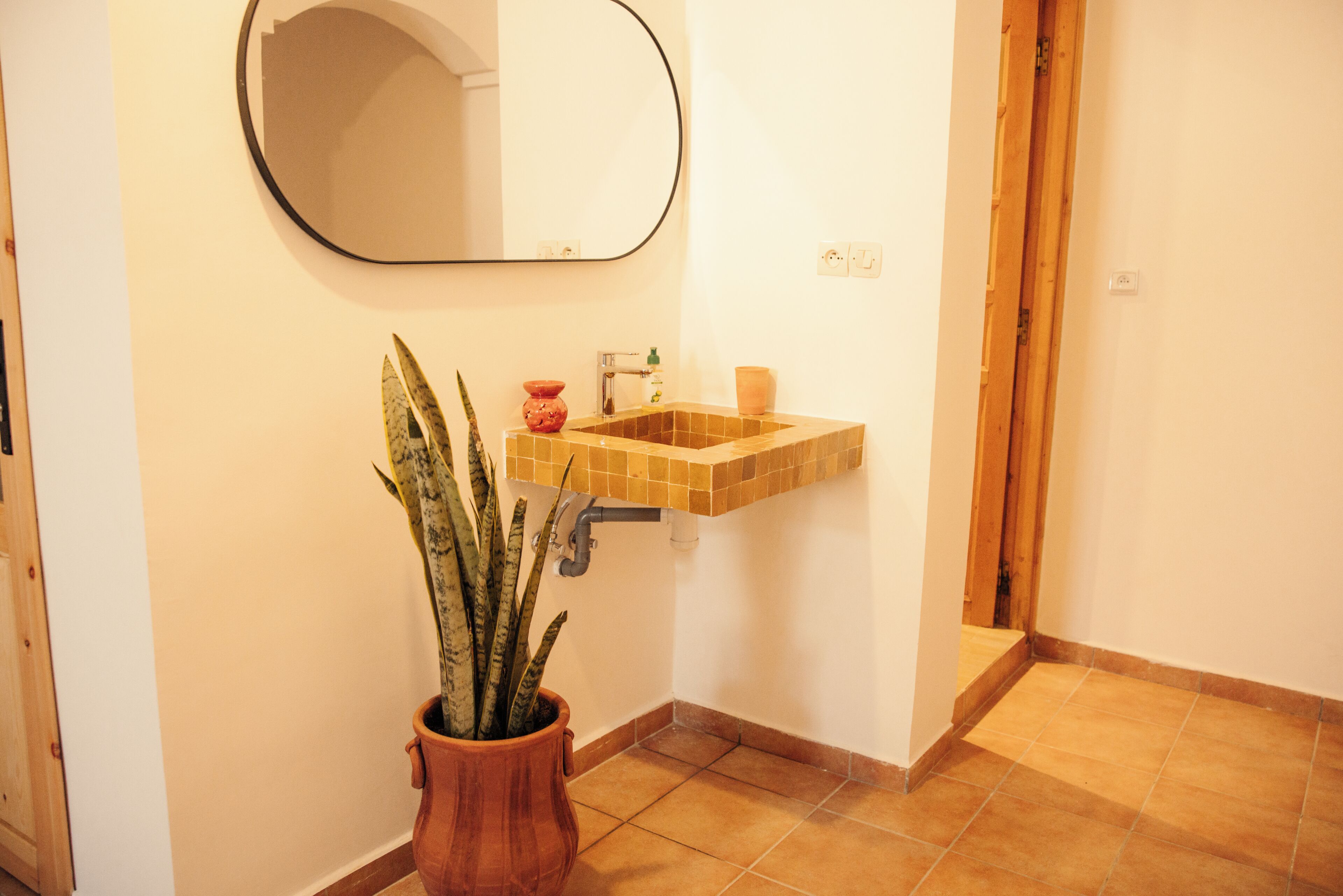 A bathroom with a tiled sink, a mirror, and a potted plant.