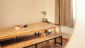 Una habitación con una mesa de comedor de madera, bancos, una lámpara colgante, una planta en maceta y una ventana con cortinas.