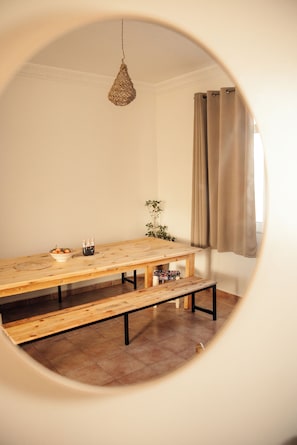 A room with a wooden dining table, benches, a hanging light fixture, a potted plant, and a window with curtains.