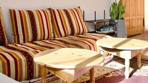 Una habitación con un sofá a rayas, dos mesas de madera, un espejo decorativo y una puerta.
