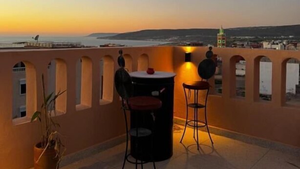 Una terraza con dos mesas y sillas, una planta en maceta y vistas de la ciudad al atardecer.