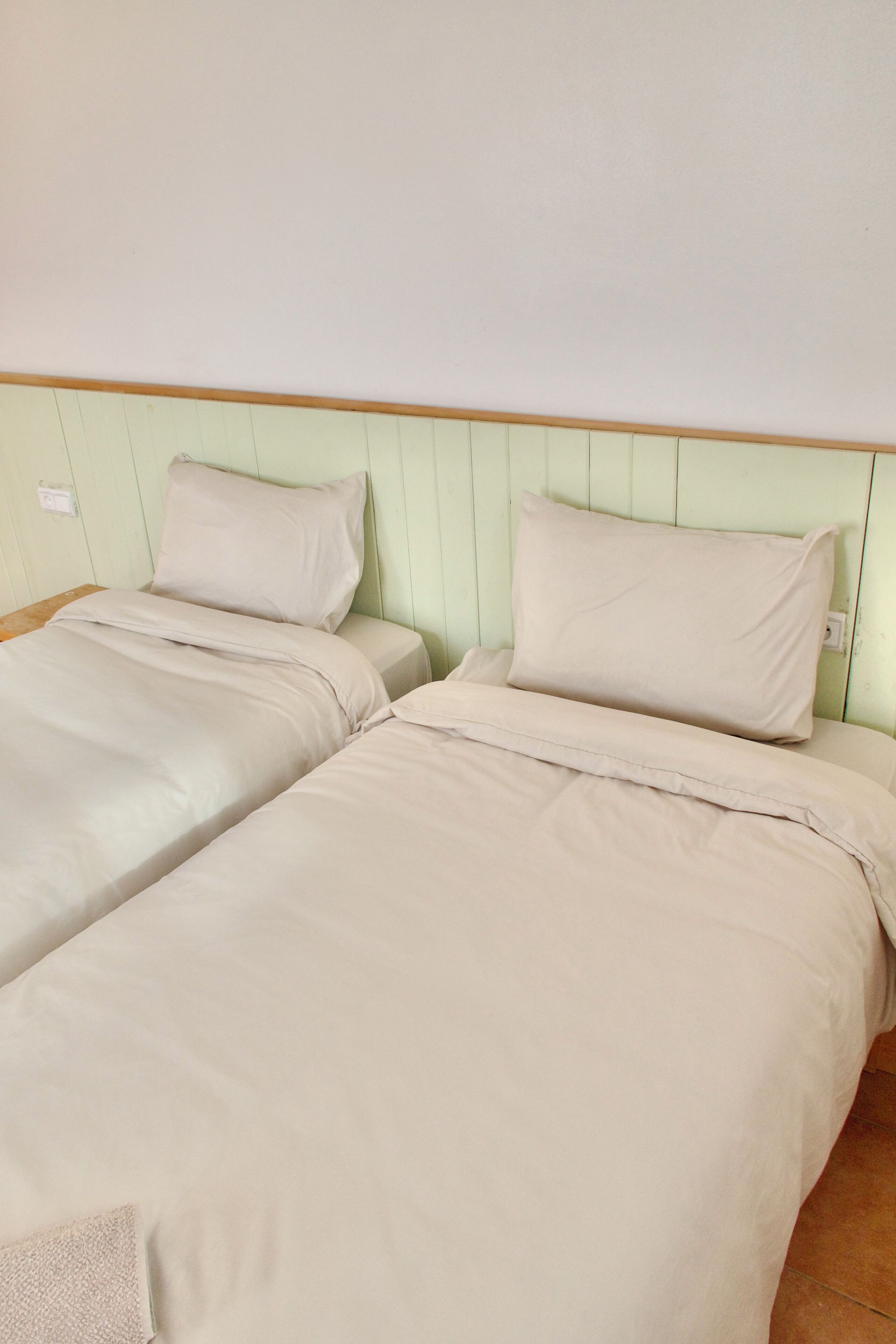 Two single beds with matching headboards and footboards, a wooden nightstand, and a light-colored wall.
