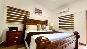 Ein Schlafzimmer mit einem hölzernen Bett, einem Nachttisch, einer Kommode und einer Deckenleuchte.
