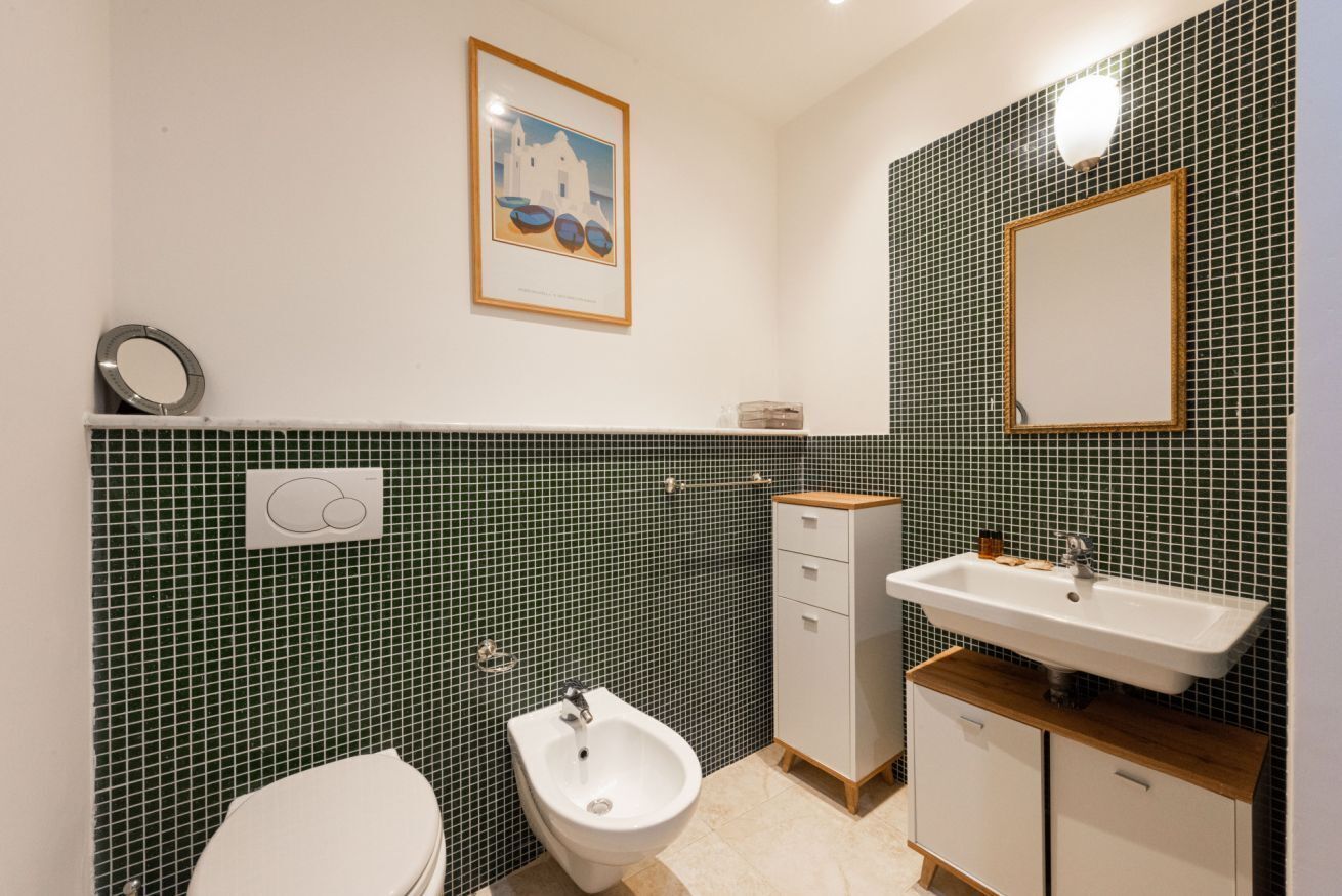 Une salle de bain équipée d’un bidet, de toilettes, d’un lavabo et d’un tableau encadré au mur.