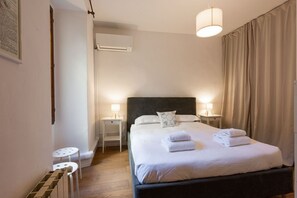 A bedroom with a large bed, bedside lamps, a small table, and an air conditioning unit. - Casa Gioia by MMega Homes and Villas (Florence)