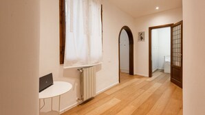Un pasillo con suelo de madera, un radiador, una mesa blanca y una puerta con un panel de vidrio.