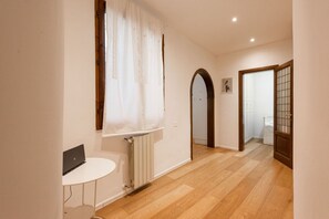A hallway with wooden flooring, a radiator, a white table, and a door with a glass panel. - Casa Gioia by MMega Homes and Villas (Florence)