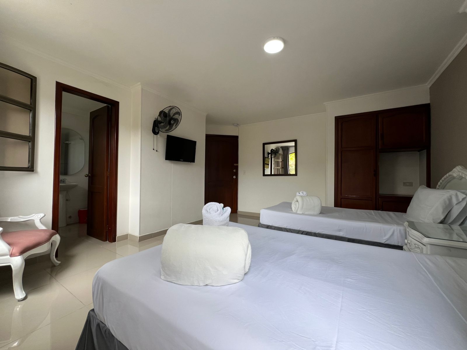 A hotel room with two beds, a TV, a fan, a mirror, and a bathroom visible through an open door.