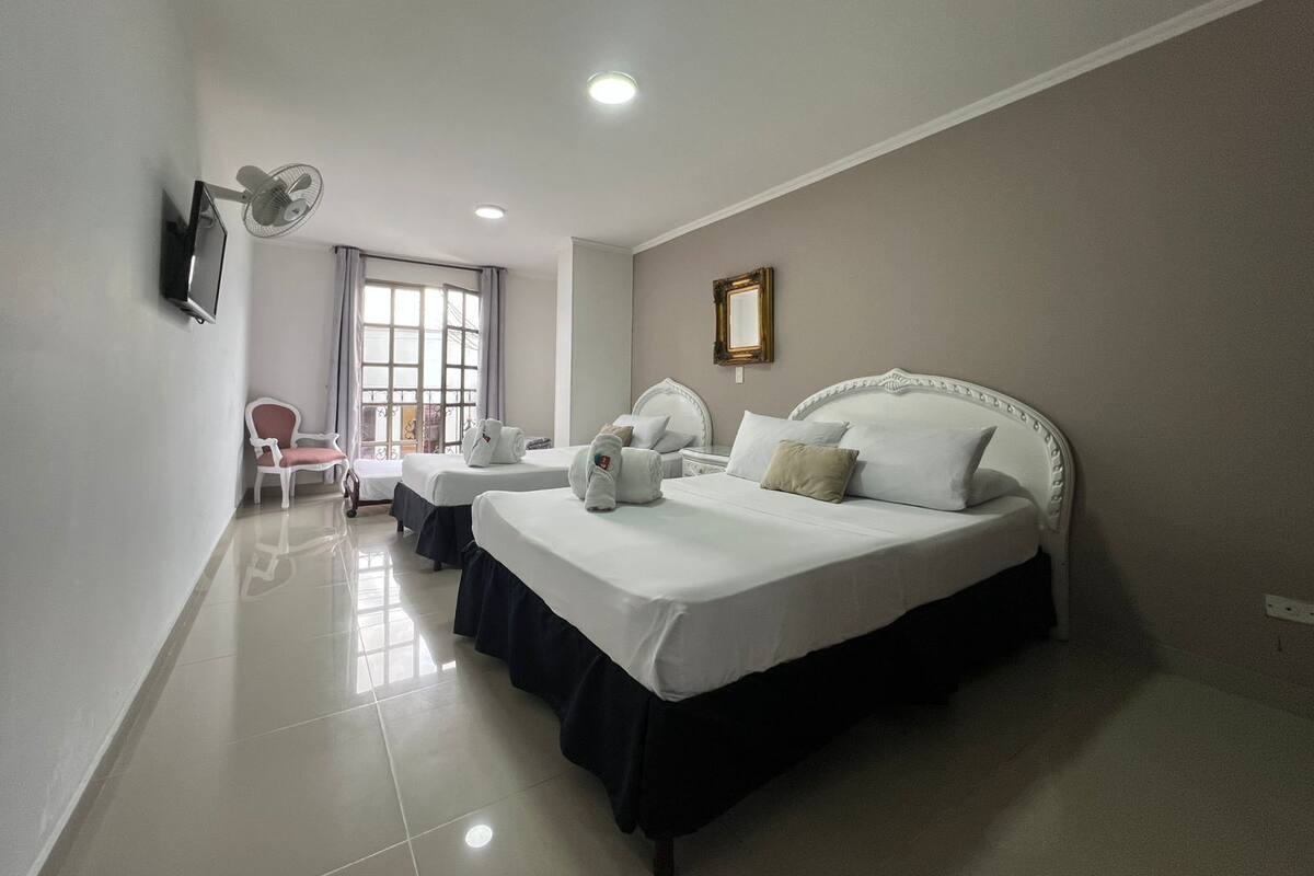 Una habitación de hotel con una cama grande, mesitas de noche, un televisor, una silla y una ventana con cortinas.