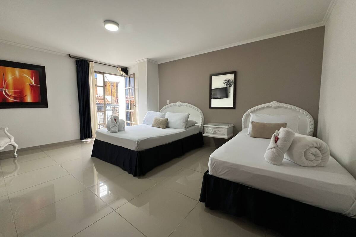 Habitación de hotel con dos camas, un televisor, un cuadro y vistas al exterior.