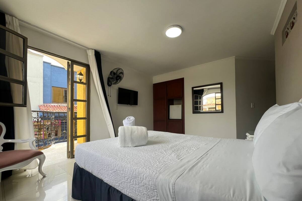 Habitación de hotel con una cama, una silla, un televisor, una ventana y una puerta que da a un balcón.