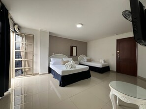 A hotel room with two beds, a small table, a TV, and a window with curtains.