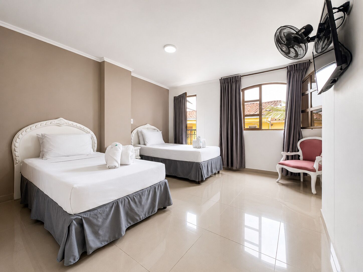 A hotel room with two beds, a TV, a chair, and a window with curtains.